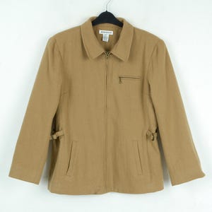 May include: A tan-colored jacket with a collar, zipper closure, and two front pockets. The jacket has long sleeves and adjustable side tabs. The jacket is hanging on a black hanger against a white background.
