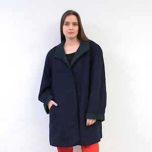 Könnte beinhalten: Ein marineblauer Mantel mit dunkelgrünem Kragen und Manschetten. Der Mantel ist ein langer, übergroßer Stil mit entspannter Passform. Das Model trägt eine rote Hose.