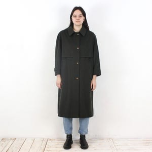 以下が含まれることがあります： 襟付きで金色のボタンが付いた、濃い緑色のロングコート。 コートは長袖で、クラシックなテーラードデザインです。 青いジーンズと黒いブーツを履いています。