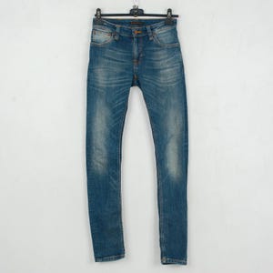 May include: Blue denim jeans hanging on a black hanger. The jeans have a classic five-pocket design, a button and zipper closure, and a faded wash. The jeans are a slim fit.