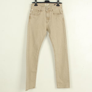 May include: Tan-colored denim jeans hanging on a black hanger against a white background. The jeans have a classic five-pocket design with a button and zipper closure. The pants are made of a sturdy denim material.