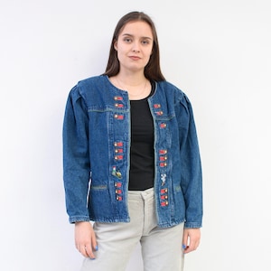 Può includere: Giacca di jeans blu con accenti decorativi rossi e gialli. La giacca ha uno scollo tondo, maniche lunghe e una chiusura con bottoni. La giacca è adornata con dettagli ricamati e piccole tasche.