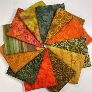 May include: A collection of 14 fabric squares in various shades of green, orange, and brown. The fabric has a batik pattern with different designs.