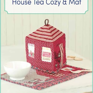 May include: A red and white house-shaped tea cosy with a red and white polka dot pattern and a red and white striped roof. The cosy is sitting on a red and white plaid mat with a white bowl next to it. The text "Sewing Goods" is on the front of the cosy. The text "English Edition!" is in a green circle on the bottom right of the image.
