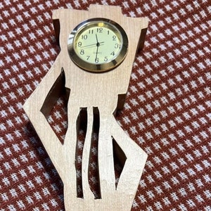 May include: A wooden clock shaped like a person standing with a clock face on the chest. The clock face has black hands and gold numbers.