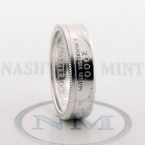 May include: A silver ring made from a 2000 quarter dollar coin. The coin features the inscription "E PLURIBUS UNUM" and "QUARTER DOLLAR".