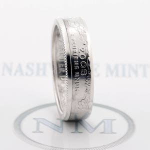 May include: A silver ring made from a 2008 United States quarter dollar coin. The coin has been cut and polished to create a smooth, comfortable band. The ring features the inscription "E PLURIBUS UNUM" and the year "2008".
