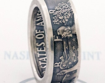 May include: A silver ring with a design of a woman holding a flag and a tree on the side. The ring is made from a US half dollar coin.