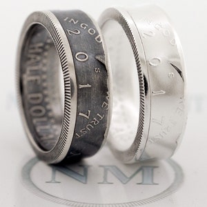 May include: Two silver half dollar rings, one with a black oxidized finish and the other with a polished finish. Both rings feature the inscription "IN GOD WE TRUST" and "HALF DOLLAR".