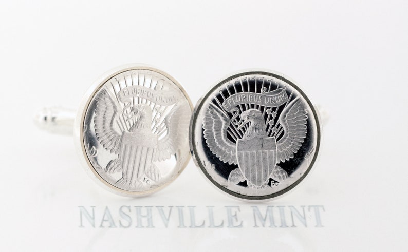 May include: A pair of silver cufflinks featuring a detailed design of the American bald eagle with the words "E Pluribus Unum" on the shield. The cufflinks are a classic and elegant accessory for any man's wardrobe.