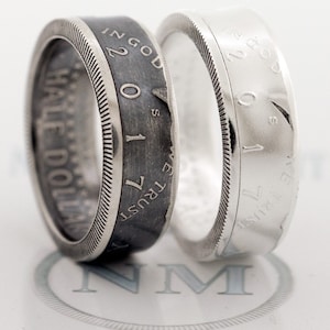 May include: Two silver half dollar rings, one with a black oxidized finish and the other with a polished finish. Both rings feature the inscription "IN GOD WE TRUST" and "HALF DOLLAR".