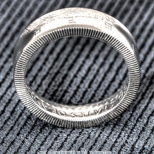 May include: Silver coin ring with the inscription "United States of America" and the year "1964". The ring is on a gray textured surface.