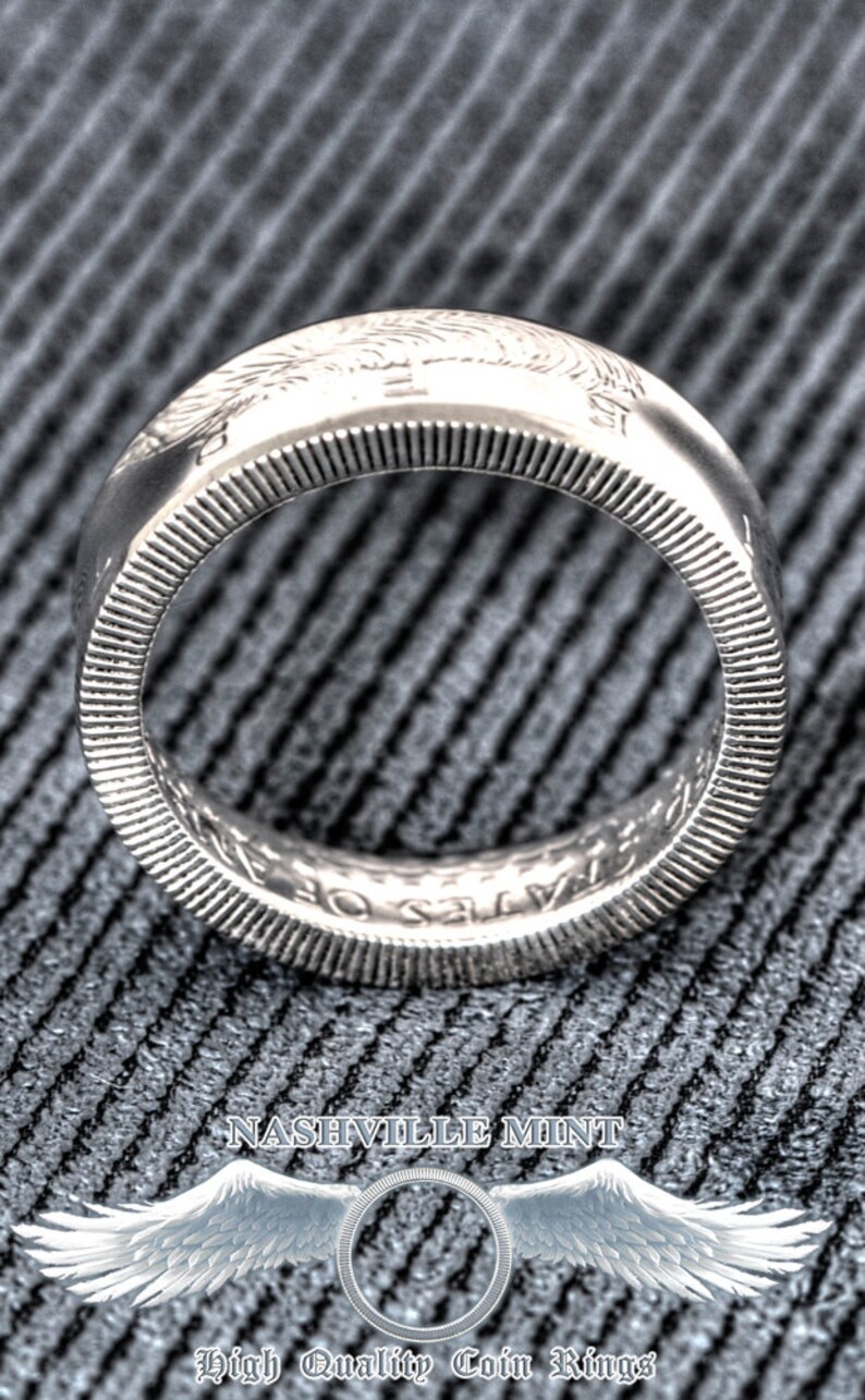 May include: Silver coin ring with the inscription "United States of America" and the year "1964". The ring is on a gray textured surface.