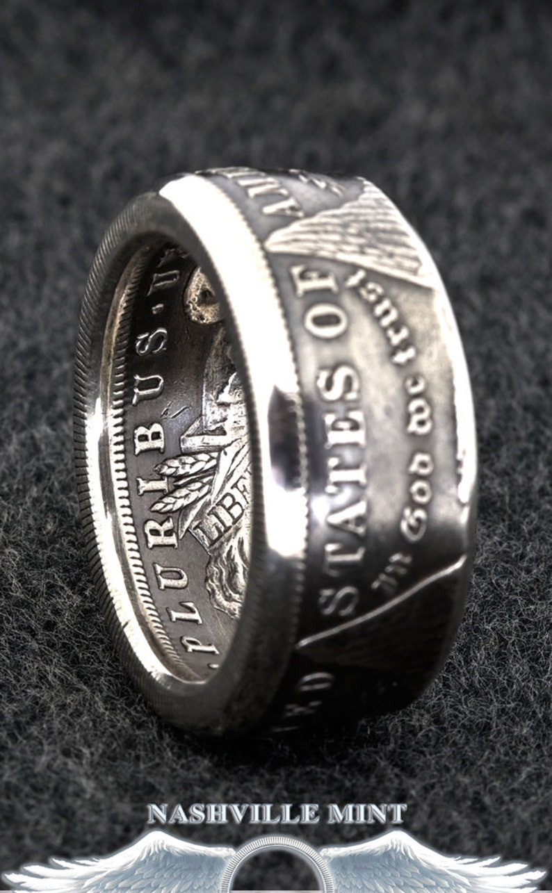 Puede incluir: Anillo de plata elaborado a partir de una moneda, con inscripciones como "In God We Trust" y "United States of America". El anillo tiene una superficie texturizada y un acabado pulido, mostrando el dise&ntilde;o original de la moneda. Una pieza de joyer&iacute;a &uacute;nica.