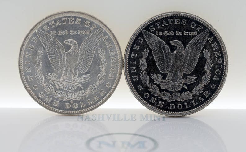 Puede incluir: Dos monedas de plata Morgan. Las monedas presentan un &aacute;guila con las alas extendidas y el texto "STATES OF AMERICA" y "ONE DOLLAR". Tambi&eacute;n son visibles las palabras "In God We Trust". Las monedas se muestran sobre una superficie blanca.