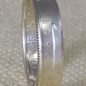 May include: Silver ring made from a 1996 United States dollar coin. The ring features the inscription "LIBERTY" and the year "1996" on the side.