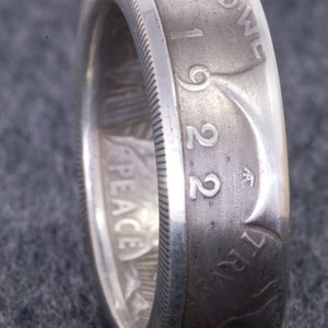 May include: A silver ring made from a 1922 Peace silver dollar coin. The ring features the inscription "IN GOD WE TRUST" and the year "1922".