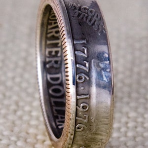 May include: A silver ring made from a quarter dollar coin. The coin has the words "In God We Trust" and "Quarter Dollar" engraved on it. The date "1776-1976" is also engraved on the coin.