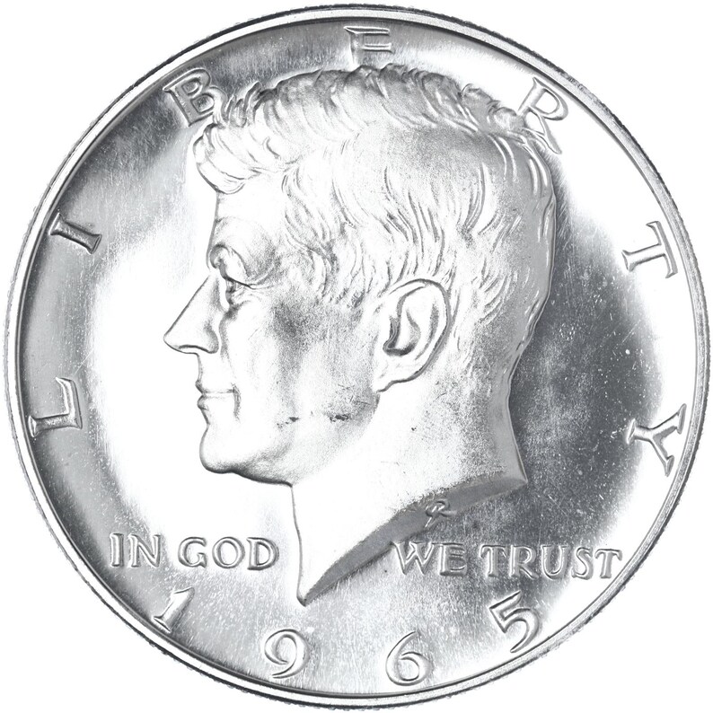 May include: Silver half dollar coin featuring a profile of John F. Kennedy with the inscription "LIBERTY" above and "IN GOD WE TRUST" below. The date "1965" is visible at the bottom.