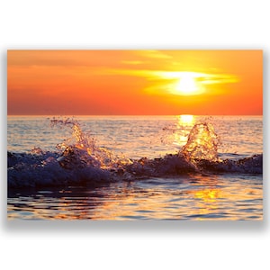 May include: A vibrant seascape captures a sunset over the ocean. The sky is ablaze with orange and yellow hues, reflecting on the water. Waves crash, creating splashes of water illuminated by the setting sun. The image evokes a sense of peace and natural beauty.