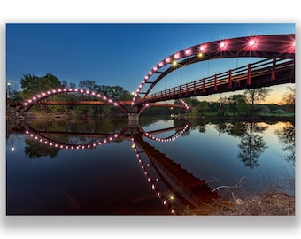 May include: A red bridge with lights spanning a river at dusk. The bridge is reflected in the water.