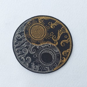 May include: A black embroidered patch with a yin yang symbol. The yin side is silver and features a stylized wave design. The yang side is gold and features a stylized sun design.