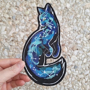Könnte beinhalten: Ein schwarzer gestickter Aufnäher mit einem Katzenmotiv und einem blauen und grünen Sternenbild.