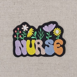 May include: A colorful embroidered patch with the word "NURSE" in a whimsical font. The letters are outlined in black and filled with different colors, including purple, yellow, orange, and blue. The patch is decorated with small embroidered flowers in various colors.