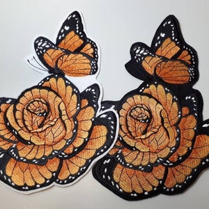 May include: Two embroidered iron-on patches featuring a rose made of monarch butterfly wings. The patches are orange and black with white accents.