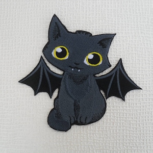 Peut inclure: Patch thermocollant en feutre noir représentant une chauve-souris de dessin animé avec des yeux jaunes et des crocs. La chauve-souris a des ailes et est assise sur ses pattes arrière.