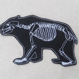May include: Black felt patch with a white embroidered outline of a bear skeleton.