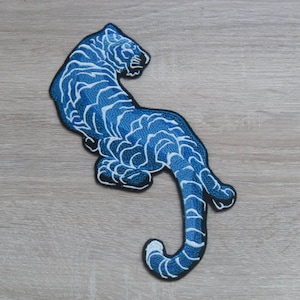 Op de afbeelding: Blauwe geborduurde strijkpatch van een tijger met witte strepen.