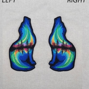 Op de afbeelding: Twee geborduurde patches met een wolfsilhouet met een kleurrijk aurora borealis-ontwerp erin. De wolf kijkt naar links en rechts, met het aurora borealis-ontwerp in tinten blauw, groen, geel, roze en paars.