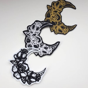 May include: Three embroidered iron-on patches featuring a crescent moon with floral designs. The patches are black with white embroidery, white with black embroidery, and black with gold embroidery.