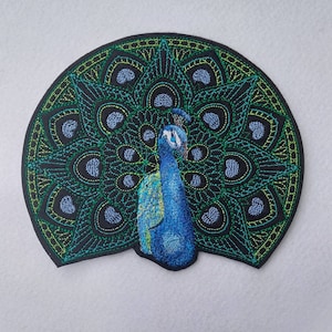 May include: Embroidered patch of a peacock with its tail feathers spread out in a mandala pattern. The peacock is blue and green with a black outline. The background is black.
