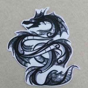 以下が含まれることがあります： 複雑なディテールが施された、黒い刺繍のアイロン接着パッチ。ドラゴンは頭をパッチの左側に向けて丸まっています。