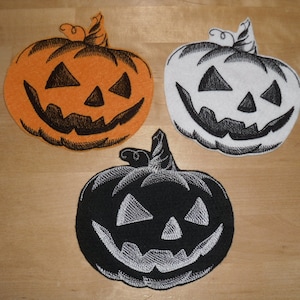 以下が含まれることがあります： ハロウィンのかぼちゃのフェルトパッチが3つ。1つはオレンジ、1つは白、もう1つは黒。それぞれに黒い刺繍の顔があります。