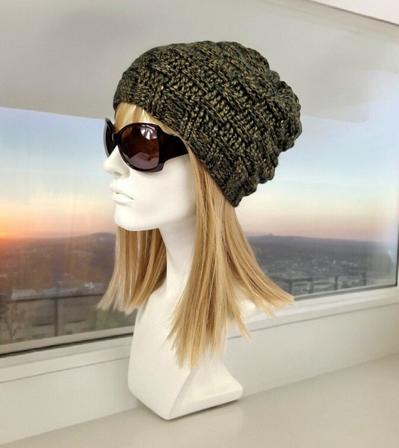 May include: A green and gold knit beanie with a slouchy fit. The beanie is worn on a mannequin with blonde hair and sunglasses.