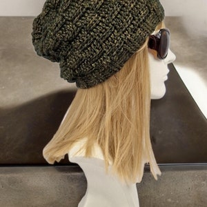 May include: A dark green and gold slouchy beanie hat with a knit texture. The hat is on a mannequin head with blonde hair.