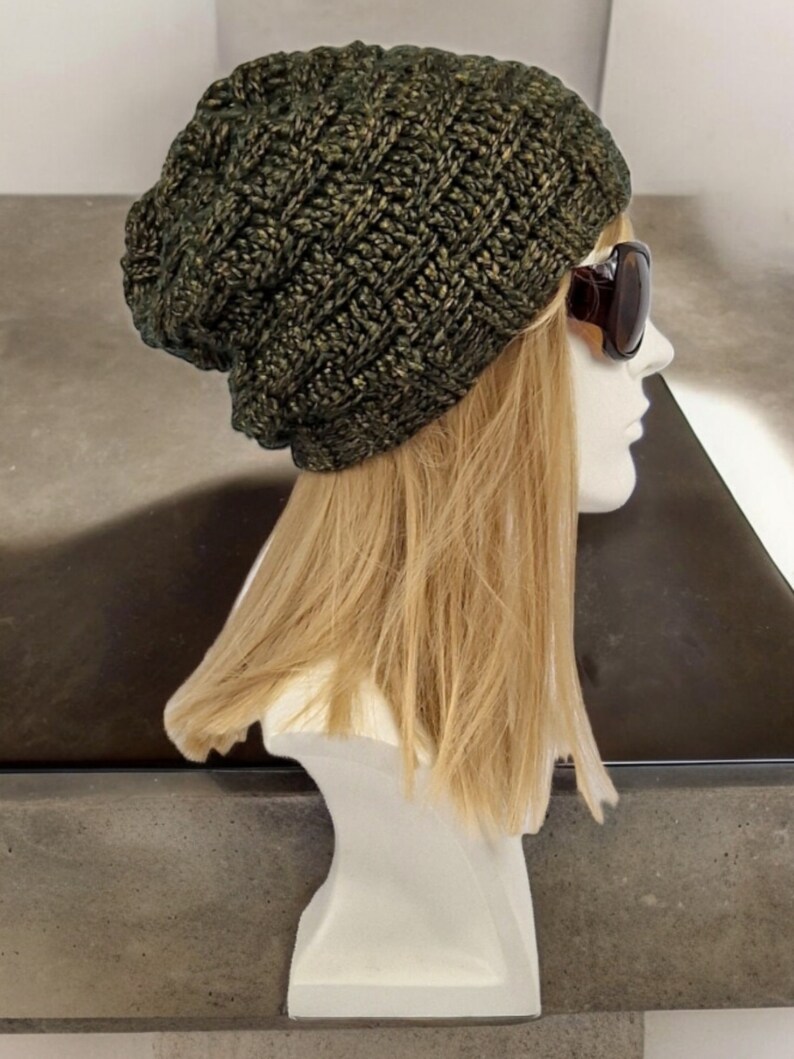May include: A dark green and gold slouchy beanie hat with a knit texture. The hat is on a mannequin head with blonde hair.
