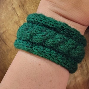 May include: A green knitted headband with a cable knit pattern.