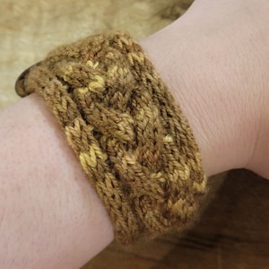May include: A brown and yellow knitted bracelet with a cable knit pattern.