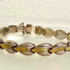 May include: A silver and gold bracelet with a heart-shaped link design. The bracelet is made of two-toned metal, with silver and gold accents.