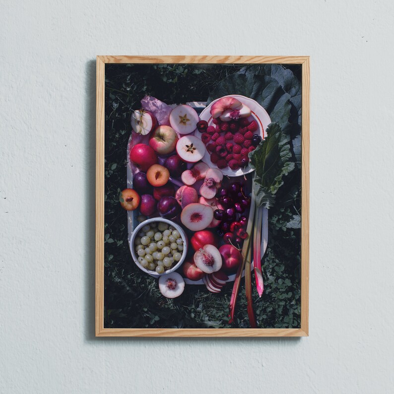 May include: A framed photograph of a still life featuring a variety of fresh fruits and berries. The fruits include red apples, plums, peaches, and cherries. The berries are raspberries and white currants. The fruits are arranged on a white plate with a red rim. The plate is surrounded by green leaves and stems.