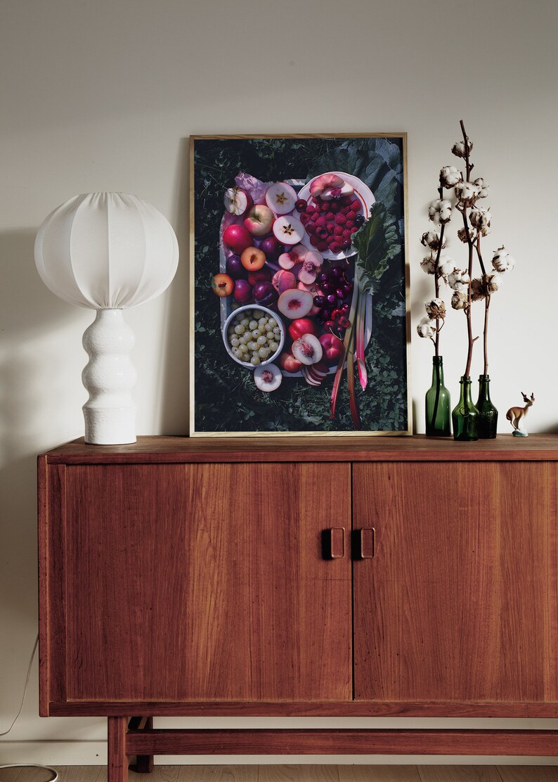 May include: A framed print of a still life featuring a variety of fresh fruit, including peaches, cherries, raspberries, and grapes, arranged on a white plate. The fruit is surrounded by green leaves and stems.