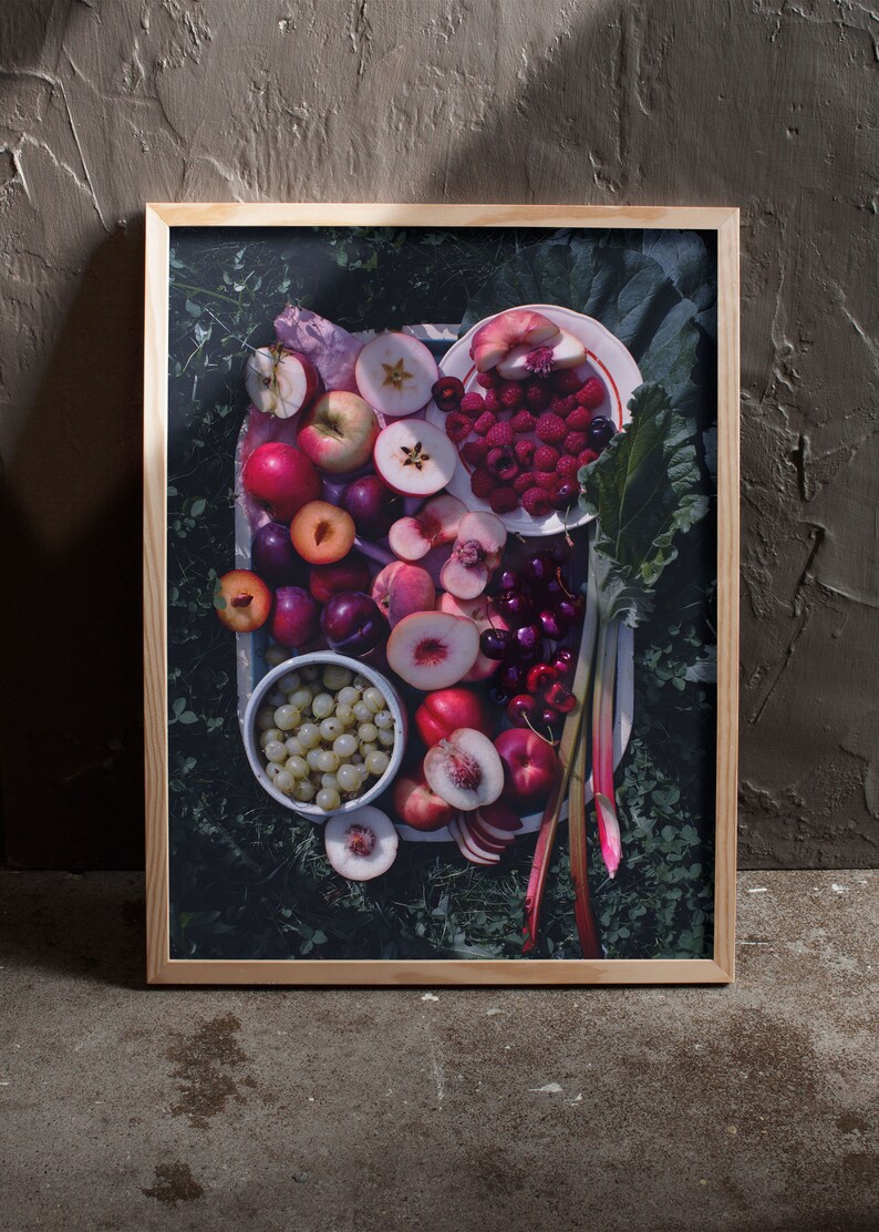 May include: A framed photograph of a tray of fresh fruit, including peaches, plums, cherries, raspberries, and apples. The fruit is arranged on a white plate with green leaves and rhubarb stalks.