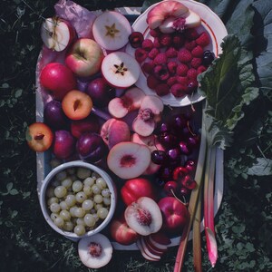 May include: A white platter filled with a variety of fresh fruit, including peaches, plums, cherries, apples, and grapes. The fruit is arranged in a colorful and appetizing display.