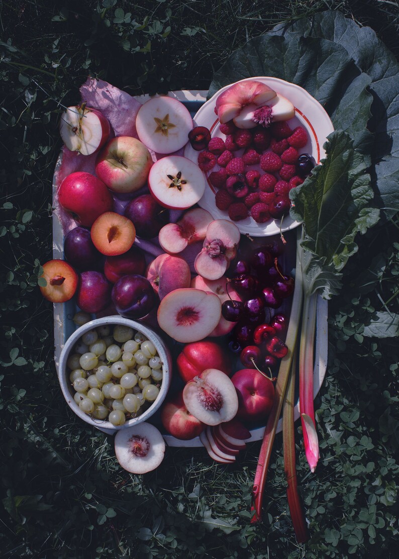 May include: A white platter filled with a variety of fresh fruit, including peaches, plums, cherries, apples, and grapes. The fruit is arranged in a colorful and appetizing display.