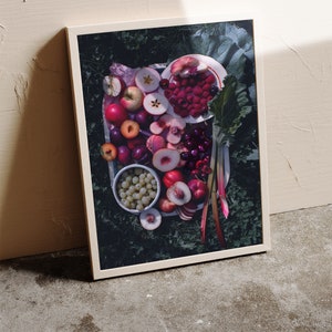 May include: A framed photograph of a still life featuring a variety of fresh fruit, including red apples, plums, peaches, cherries, and raspberries, arranged on a white plate with green leaves and rhubarb stalks.
