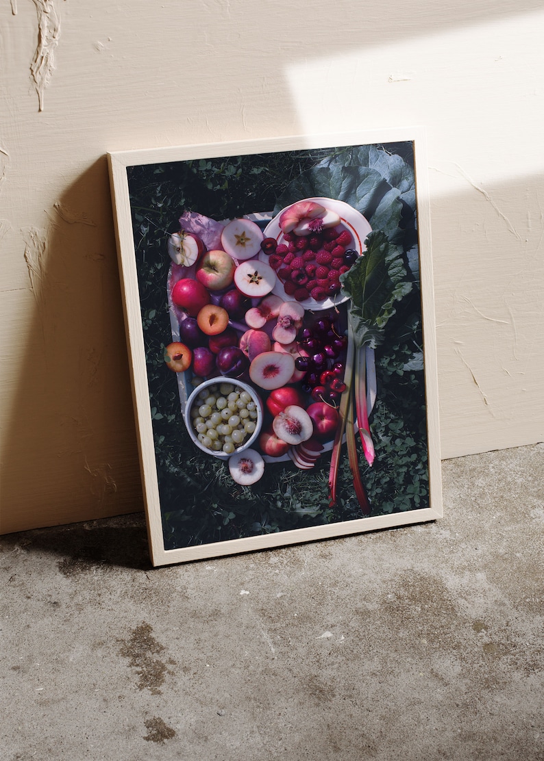 May include: A framed photograph of a still life featuring a variety of fresh fruit, including red apples, plums, peaches, cherries, and raspberries, arranged on a white plate with green leaves and rhubarb stalks.